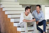Sorridenti amici maschi seduti su gradini con vino rosso — Foto stock