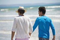 Homens relaxados andando na praia com mar ondulado — Fotografia de Stock