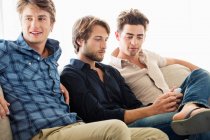 Три друга-мужчины сидят вместе на диване — стоковое фото