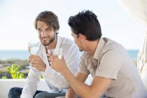 Lächelnde männliche Freunde genießen Weißwein im Freien — Stockfoto