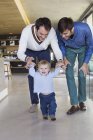 Genitori lgbt felici aiutare il figlio a camminare a casa — Foto stock