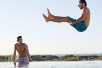 Мужчина прыгает в бассейн с другом, стоящим у бассейна — стоковое фото