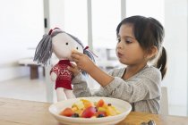 Menina alimentando salada de frutas para boneca na cozinha — Fotografia de Stock