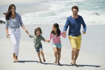 Счастливая семья, гуляющая по песчаному пляжу, держась за руки — стоковое фото