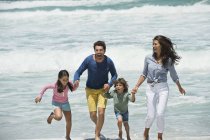 Счастливая семья, бегущая по пляжу с волнами моря — стоковое фото