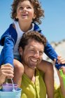 Man carrying his son on shoulders on the beach — Stock Photo
