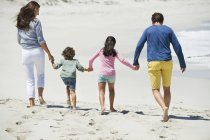 Vista trasera de la familia caminando en la playa de arena - foto de stock