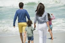 Famille heureuse marchant sur la plage avec mer ondulante sur le fond — Photo de stock
