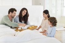 Дети, подающие чай счастливым родителям в постели — стоковое фото