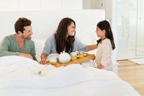 Mädchen serviert ihren Eltern Tee auf dem Bett — Stockfoto