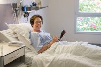 Portrait of smiling woman writing in magazine on hospital bed — Stock Photo