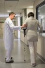 Médico masculino assistindo paciente feminino em muletas no hospital — Fotografia de Stock