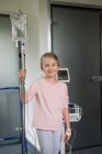Портрет улыбающейся блондинки пациентки, стоящей в больнице с капельницей внутривенно — стоковое фото