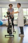 Fisioterapeuta que ayuda a un paciente a montar en bicicleta estática - foto de stock