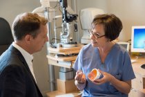 Optometrista mujer discutiendo con paciente en clínica - foto de stock