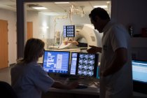 Ärzte untersuchen Scan am Computer mit Patient am MRI-Scanner im Hintergrund — Stockfoto