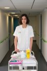 Portrait of female nurse with serving trolley in hospital corridor — Stock Photo