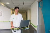 Retrato de una enfermera usando un portátil en el pasillo del hospital - foto de stock