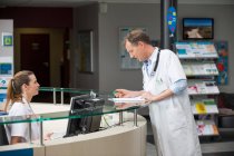 Male doctor discussing paper with receptionist at hospital reception desk — Stock Photo