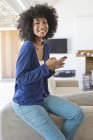 Lächelnde Frau benutzt Handy, während sie sich zu Hause auf Sofa lehnt — Stockfoto