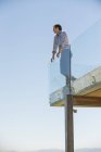 Задумчивый человек стоит на террасе и смотрит в сторону голубого неба — стоковое фото