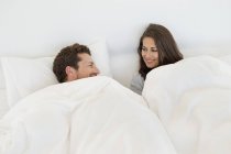 Улыбающаяся пара отдыхает на кровати и смотрит друг на друга — стоковое фото