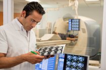 Médico varón examinando informe de resonancia magnética en sala de exploración médica - foto de stock