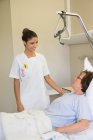 Female nurse attending patient on hospital bed — Stock Photo