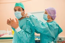 Cirurgiã mulher ajudando um cirurgião masculino vestindo roupas protetoras — Fotografia de Stock