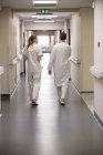Vista trasera de los médicos caminando por el pasillo de un hospital - foto de stock