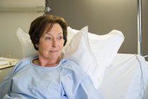 Усміхнена зріла жінка лежить в лікарняному ліжку і дивиться геть — стокове фото