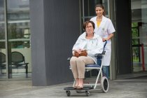 Женщина-врач толкает пациента, сидящего в кресле — стоковое фото
