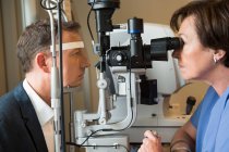 Female optometrist examining male eyes — Stock Photo