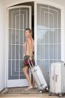 Улыбающаяся женщина с багажом стоит у дверей дома — стоковое фото