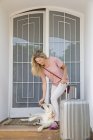 Щаслива жінка з багажем грає з собакою біля дверей будинку — стокове фото