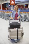Mujer rubia sonriente llevando equipaje en el aeropuerto - foto de stock