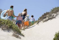 Задний вид на семью, идущую по песчаному пляжу — стоковое фото