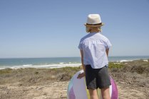 Вид сзади на девочку, стоящую с пляжным мячом на берегу — стоковое фото
