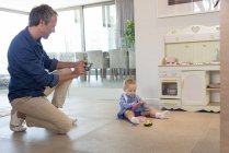 Зрелый мужчина фотографирует маленькую дочь, играющую с игрушками — стоковое фото