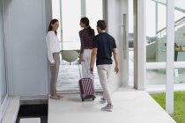 Happy woman welcoming friends with suitcase at doorway — Stock Photo