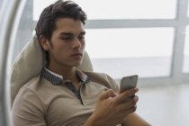 Молодий чоловік сидить у кріслі і використовує смартфон — стокове фото