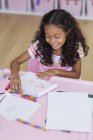 Smiling little girl doing homework at pink table — Stock Photo