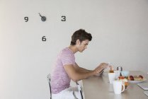 Молодий чоловік використовує мобільний телефон за столом на кухні — стокове фото