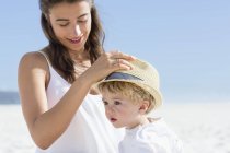 Femme mettant un chapeau sur la tête de bébé sur la plage — Photo de stock