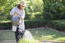 Жінка в солом'яному капелюсі поливає рослини в літньому саду — стокове фото