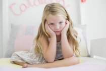 Portrait of cute little girl sitting on bed with head in hands — Stock Photo