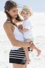Donna felice che porta il bambino sulla spiaggia — Foto stock