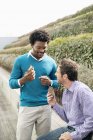 Male friends eating sandwiches on boardwalk in nature — Stock Photo