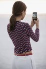 Молода жінка фотографує зі смартфоном на березі річки — стокове фото