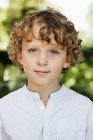 Крупним планом усміхнений хлопчик з кучерявим волоссям у білій сорочці — стокове фото